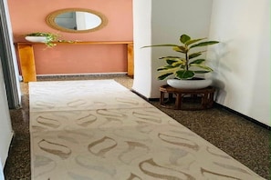 A hallway with a patterned carpet, a round mirror on the wall, a wooden bench, and a potted plant. - A very quiet apartment in the heart of downtown. (Alger Centre)