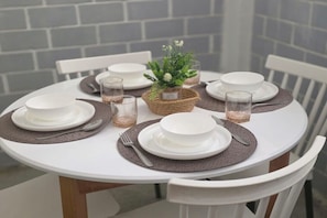 A round dining table with white chairs, set with white plates, cutlery, and glassware, centered with a woven basket containing a small plant. - A very quiet apartment in the heart of downtown. (Alger Centre)