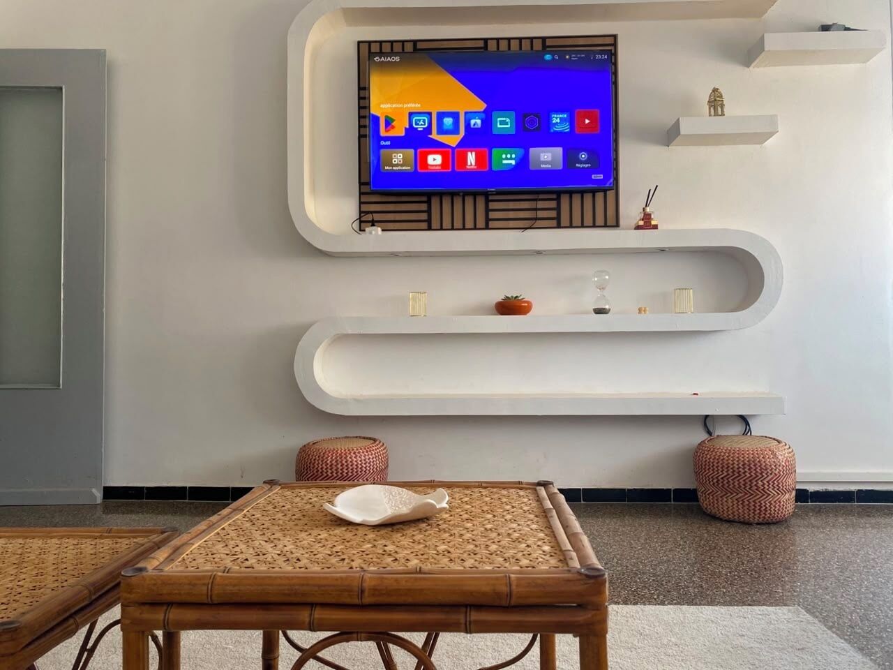 A modern interior with a flat-screen TV mounted on the wall, a white console table, and a bamboo table with a white tray.