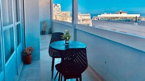 Un balcó amb taula i cadires, plantes en testos i vista a edificis.