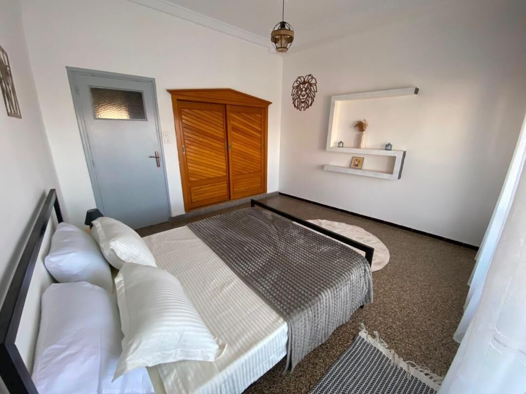 A bedroom with a bed, a wardrobe, a mirror, and a wall-mounted shelf.