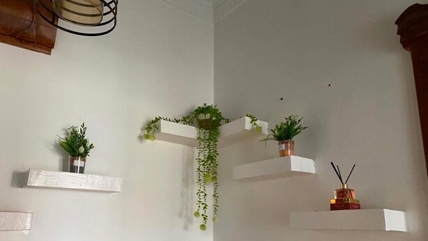 Un racó amb prestatgeries flotants blanques, algunes amb plantes, i una paret de pedra.