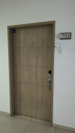 A wooden door with a keypad lock, a number plate, and a wall-mounted light fixture. - 3-bedroom Apartment in San Salvador escalon with AC and fitness room (San Salvador)