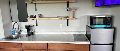 A compact kitchen with a sink, coffee maker, microwave, and a small refrigerator.
