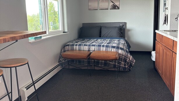 Een slaapkamer met een bed, twee krukken, een raam en uitzicht op groen.