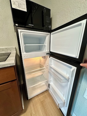 Un réfrigérateur ouvert, doté de plusieurs étagères, avec un four à micro-ondes placé au-dessus.