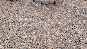 A charcoal grill with food being cooked, surrounded by a gravel area.