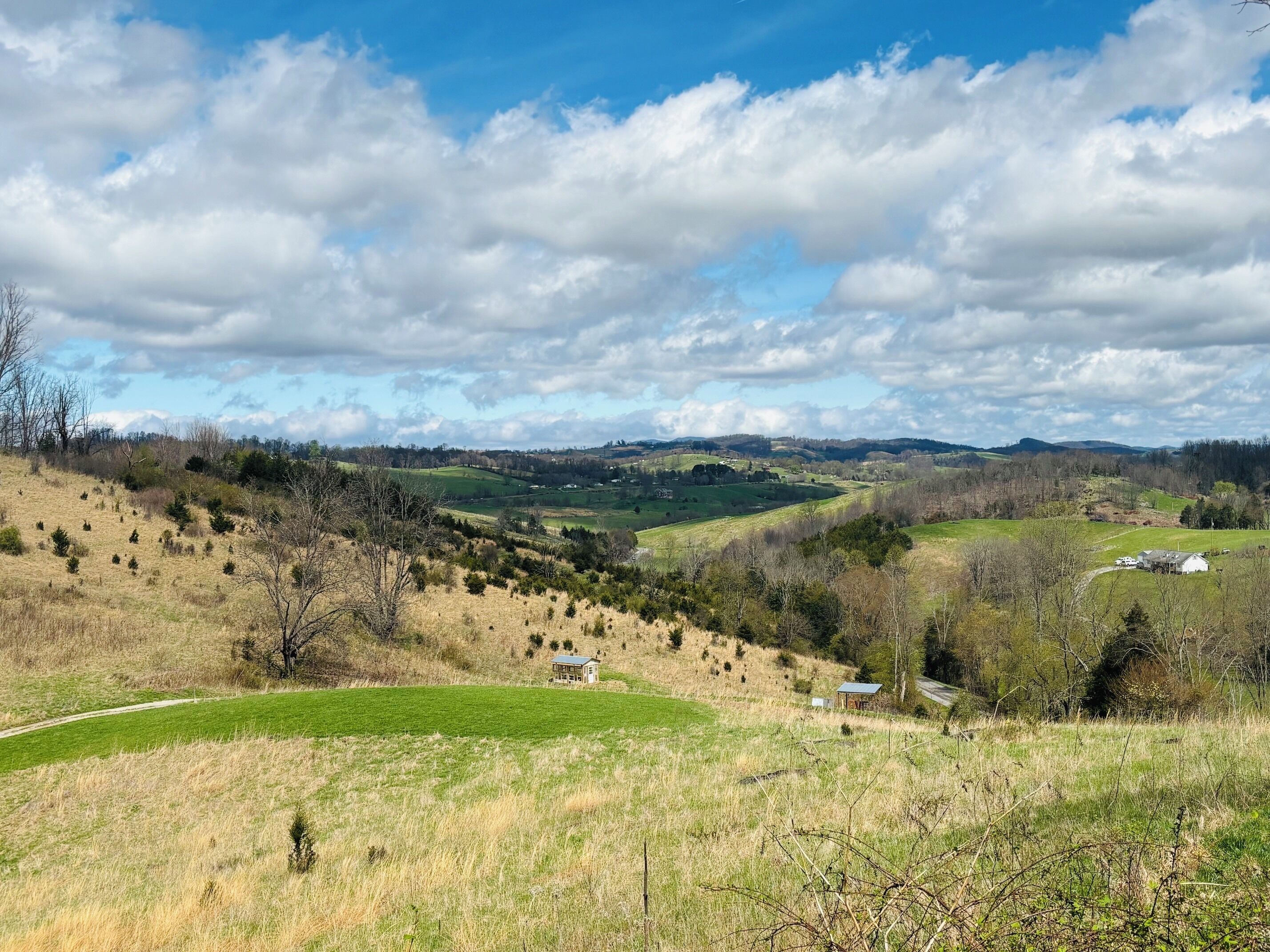 A rural landscape with rolling hills, scattered trees, and a few buildings.