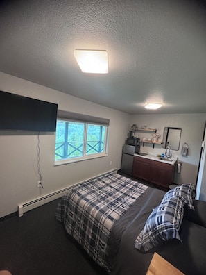 Habitación compacta con cama, una kitchenette pequeña, ventana con vistas y una lámpara de techo.