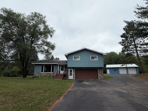 A two-story house with a garage, a front porch, and a driveway leading to the garage. - Spacious Wisconsin Northwoods Escape -Private Fire Pit and Close Water Access (Porterfield)