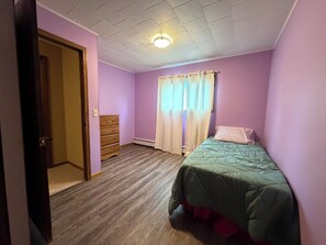 A bedroom with a wooden dresser, a bed with a green bedspread, and a window with sheer curtains. - Spacious Wisconsin Northwoods Escape -Private Fire Pit and Close Water Access (Porterfield)