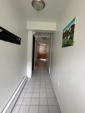 A hallway with a tiled floor, a black coat rack, and a painting on the wall. - Spacious Wisconsin Northwoods Escape -Private Fire Pit and Close Water Access (Porterfield)