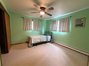 A bedroom with a bed, a ceiling fan, two windows with curtains, and a painting on the wall. - Spacious Wisconsin Northwoods Escape -Private Fire Pit and Close Water Access (Porterfield)