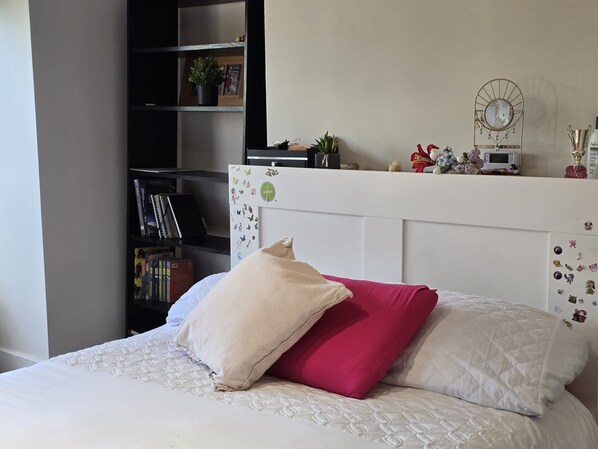 Quarto com uma cama, uma estante e uma prateleira na parede com objetos decorativos.