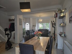 Uma ampla sala de jantar com uma grande mesa de madeira, cadeiras de couro preto e um candelabro.
