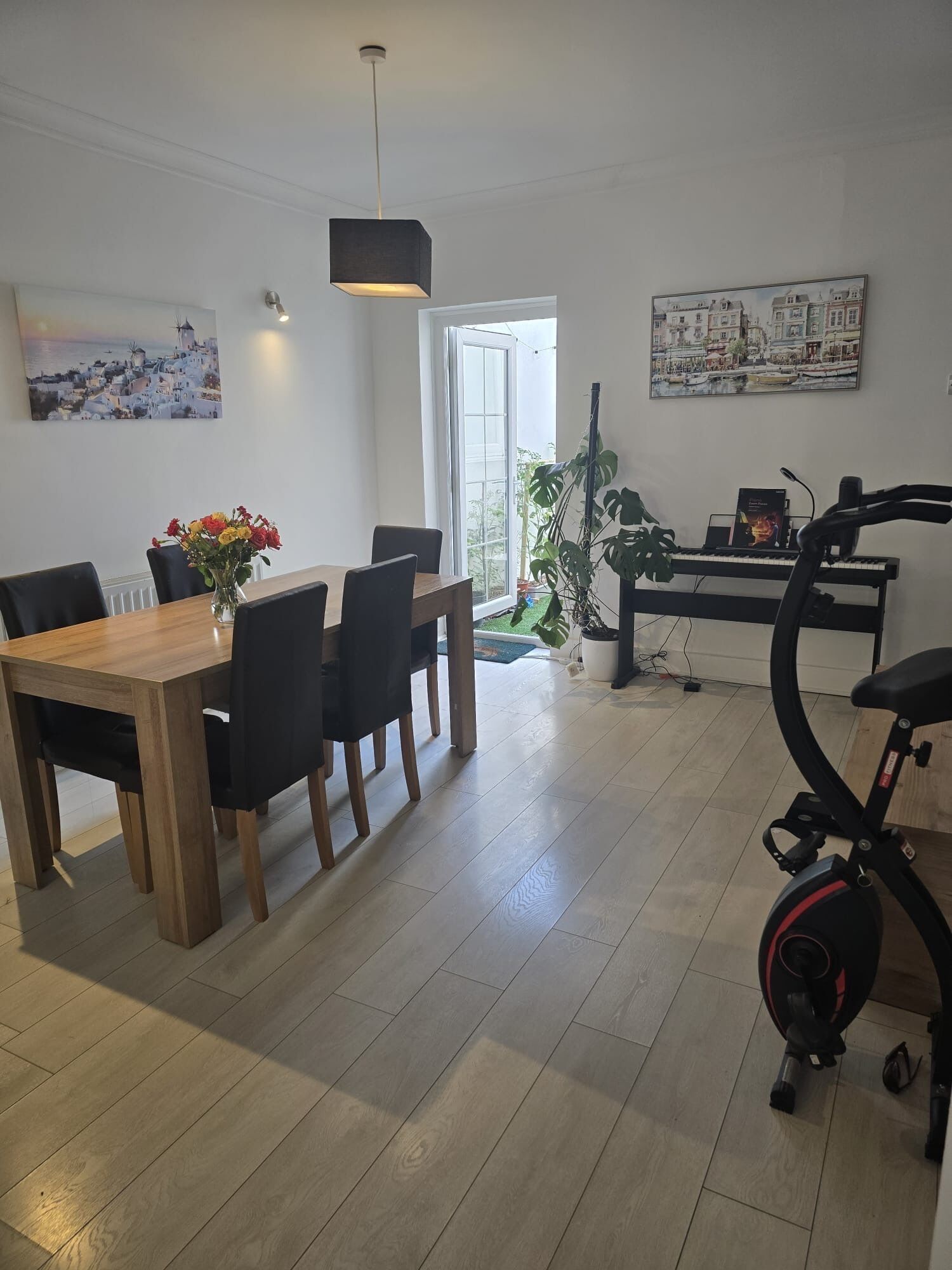 A dining area with a wooden table and chairs, a potted plant, a treadmill, and a piano.