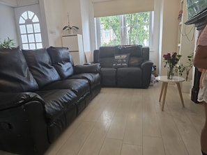 Uma sala de estar com um sofá de couro preto, uma mesa de centro branca e uma televisão.