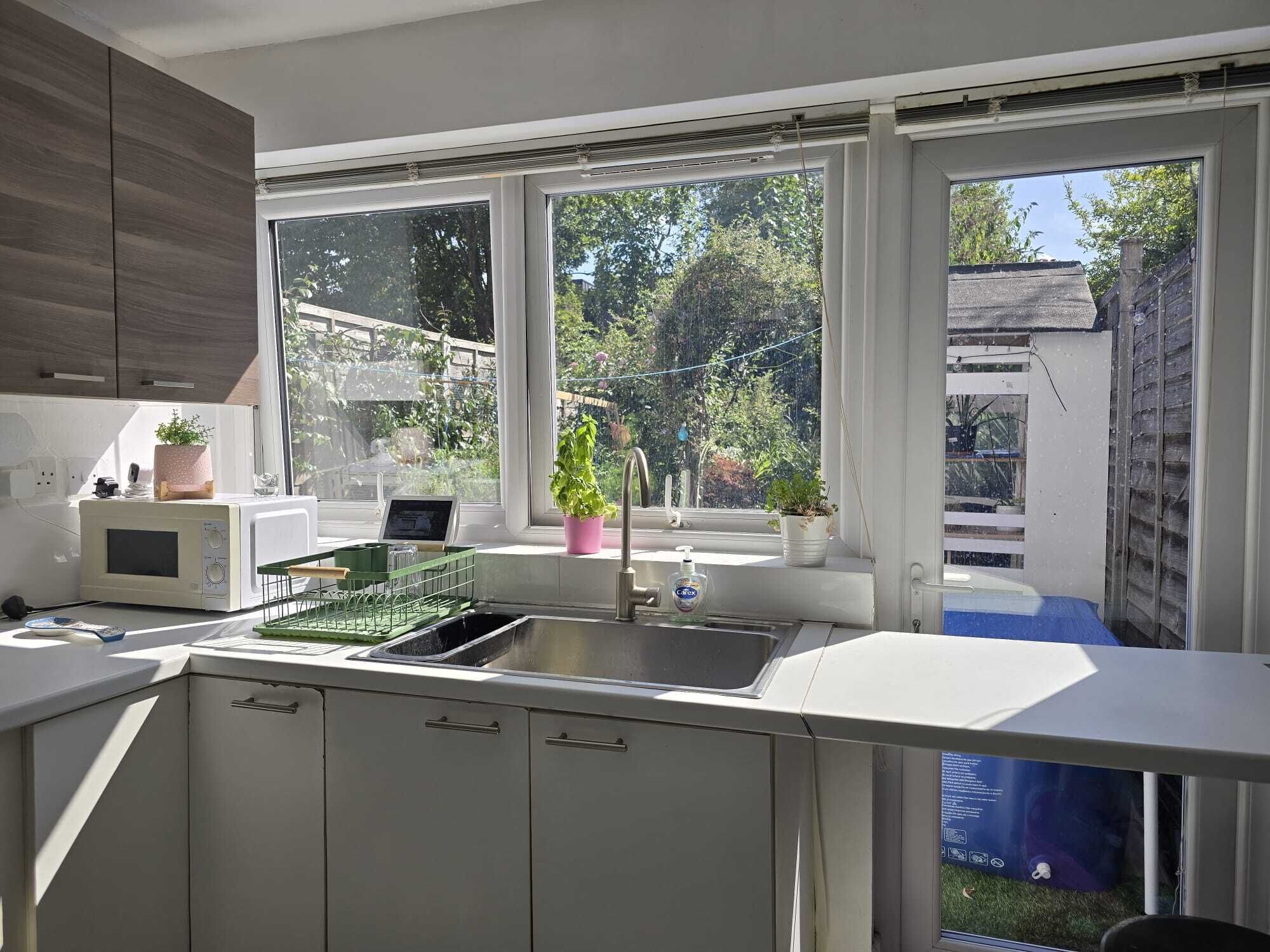 A kitchen with a built-in sink, a microwave, and cabinets. There are windows providing natural light and a view of the outside.