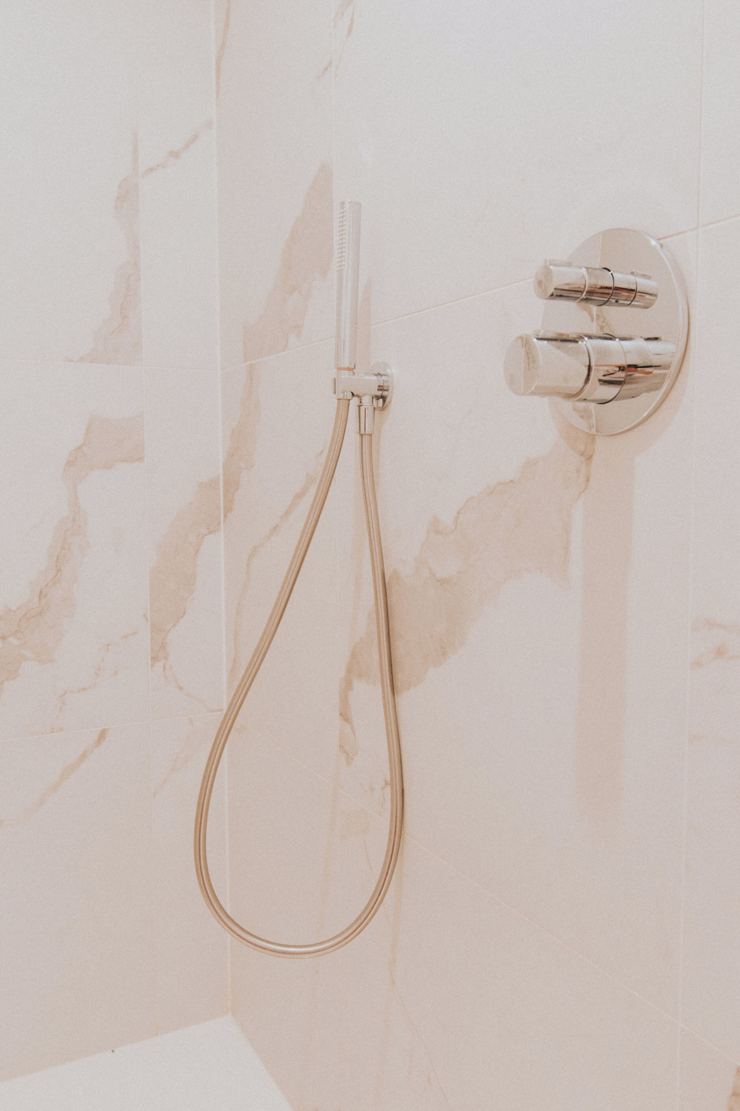 Une salle de bain avec un mur en marbre, une douche équipée d’un pommeau flexible et d’un robinet mural.