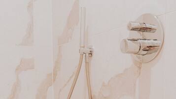 Une salle de bain avec un mur en marbre, une douche équipée d’un pommeau flexible et d’un robinet mural.