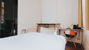 A hotel room with a bed, a small table, a chair, a fireplace, and a window with curtains. - Josephine: romantic room in a historic mansion, heart of Antwerp (Antwerp)