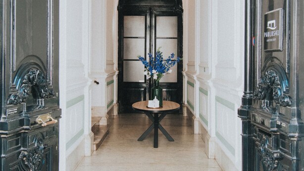 A hallway with ornate black doors, a round table with a vase of flowers, and a chandelier. - Josephine: romantic room in a historic mansion, heart of Antwerp (Antwerp)