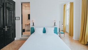 Ett hotellrum med en säng, en stol, ett litet bord, en dörr och ett fönster med gardiner.