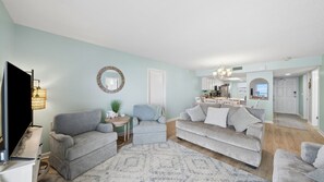 Ein Wohnzimmer mit einem grauen Sofa, einem runden Spiegel und einem Flachbildfernseher.