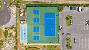 An aerial view of a tennis court with a parking lot and surrounding greenery.