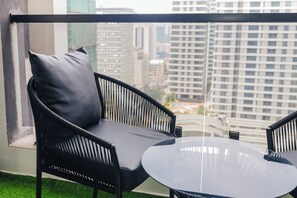 Ein Balkon mit einem schwarzen Korbstuhl und einem runden Tisch, mit Blick auf eine Skyline mit hohen Gebäuden.