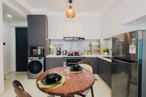 Een moderne keuken met een inbouwmagnetron, oven en wasmachine, een houten eettafel met stoelen, en een roestvrijstalen koelkast.