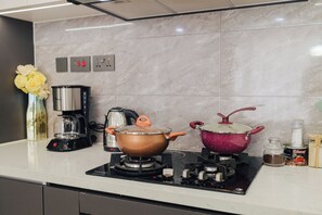A kitchen with a gas stove, two pots, a coffee maker, and a vase with flowers.