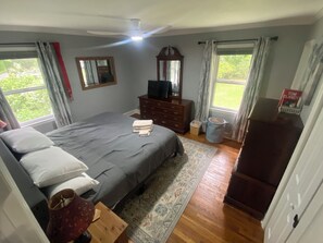 Ein Schlafzimmer mit Bett, Kommode, Fernseher und Fenstern.