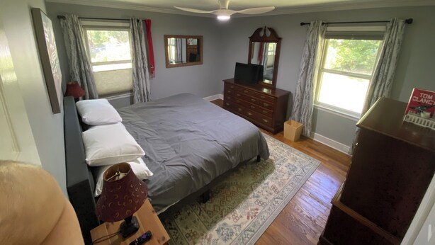 A bedroom with a bed, dresser, mirror, and windows.
