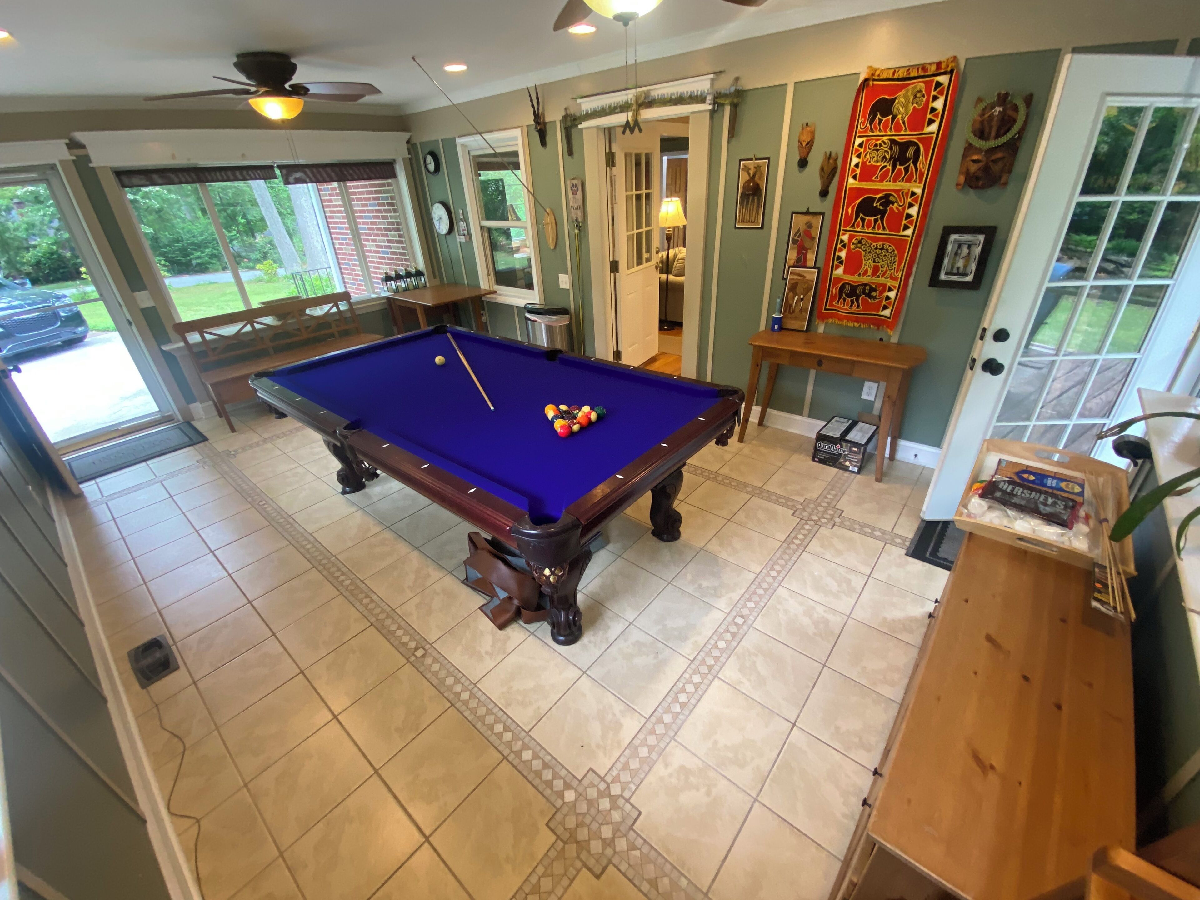 Een pooltafel met een blauwe viltbekleding, een houten bank en een deur met decoratief paneel.