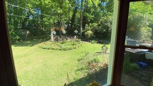 A view through a window of a well-maintained garden with a lawn, a small tree, and a patio area.