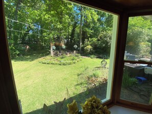 A view through a window of a well-maintained garden with a lawn, a small tree, and a patio area.