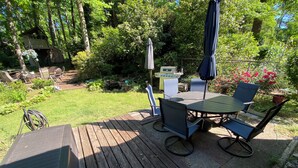 A wooden deck with a table and chairs, surrounded by lush greenery and a small shed.