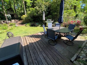 A wooden deck with a table and chairs, surrounded by lush greenery and a small shed.