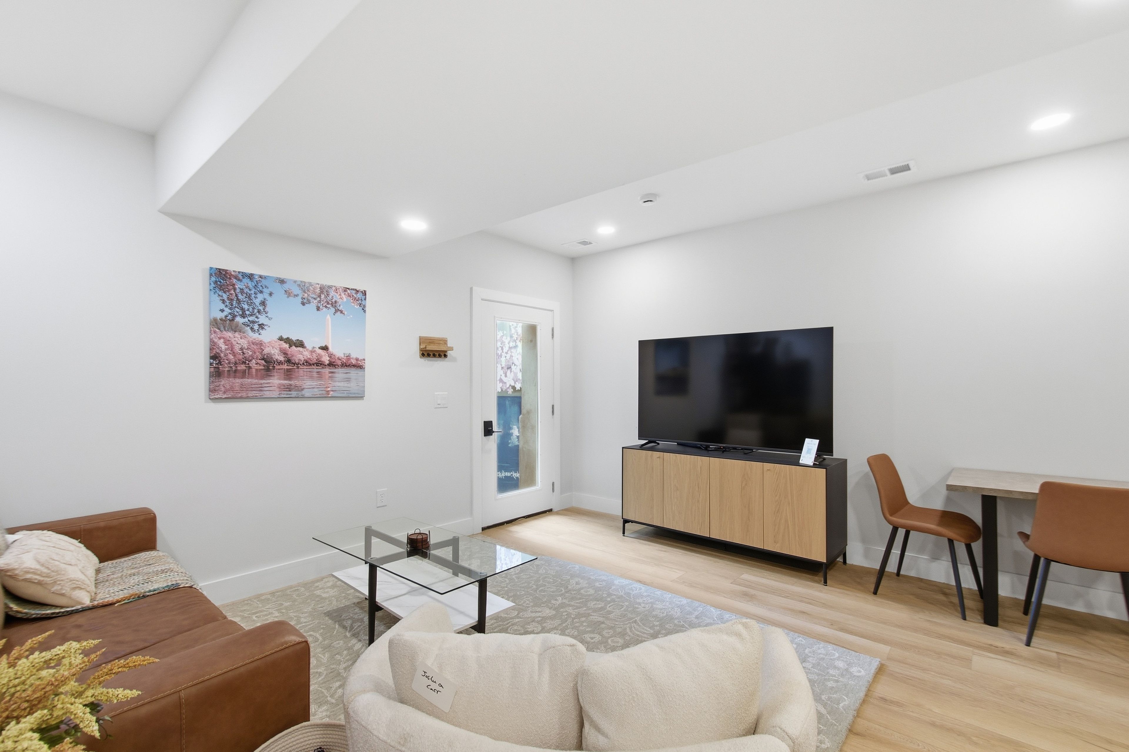 A modern living room with a sofa, a glass coffee table, a TV, and a dining area with chairs.