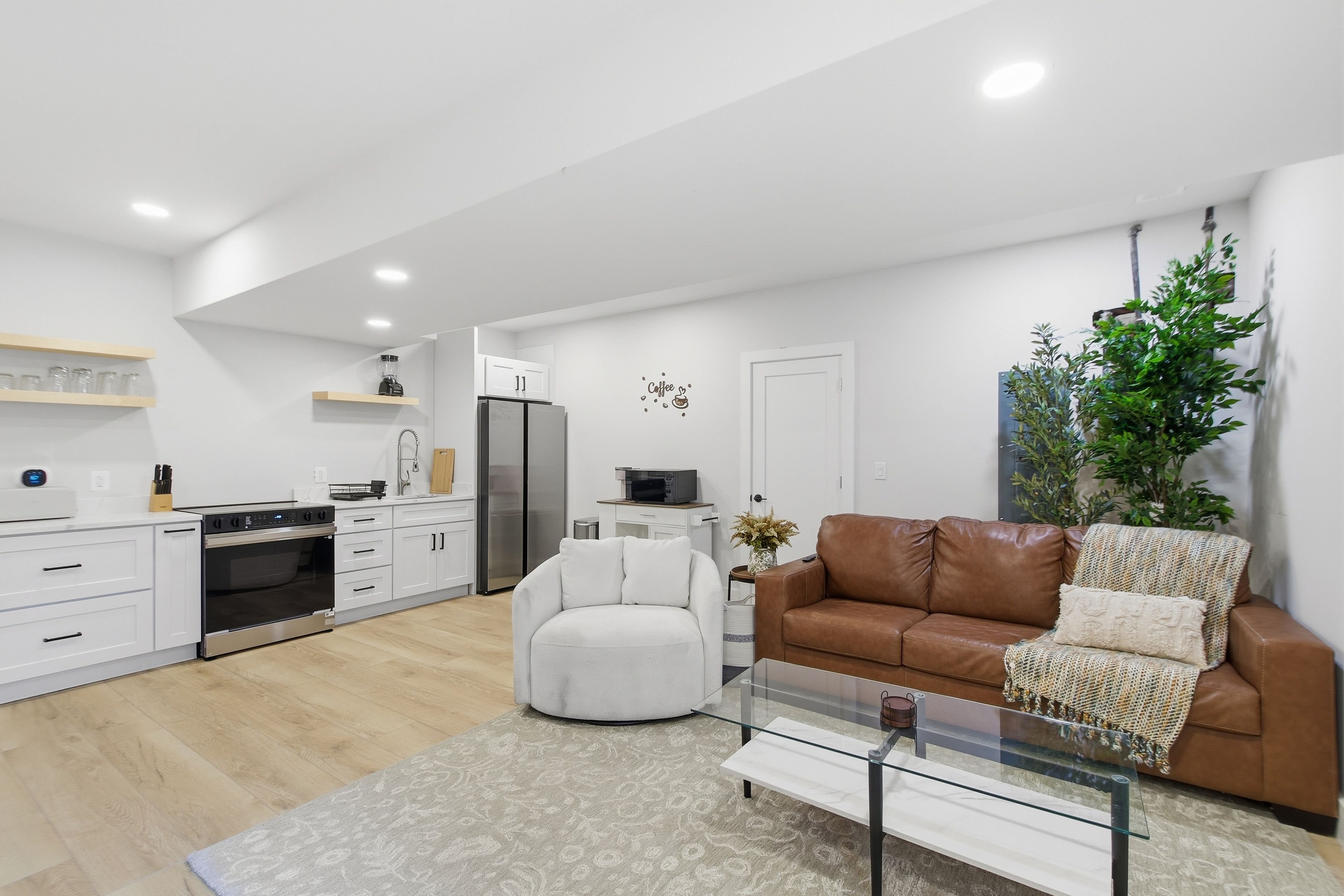 Un salon moderne avec un canapé en cuir marron, une table basse en verre et un fauteuil blanc.