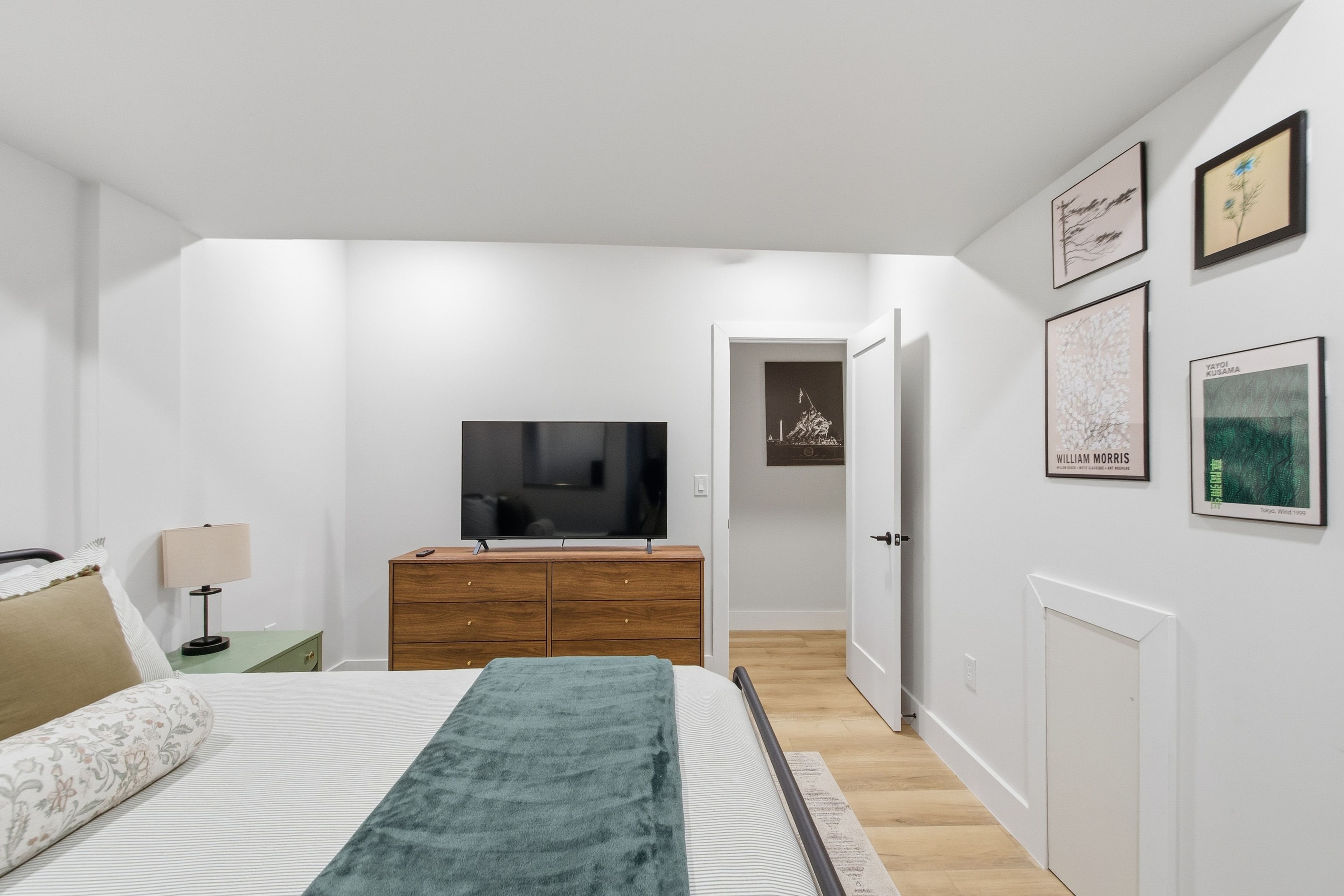 A modern bedroom with a bed, a dresser, a television, and artwork on the walls.