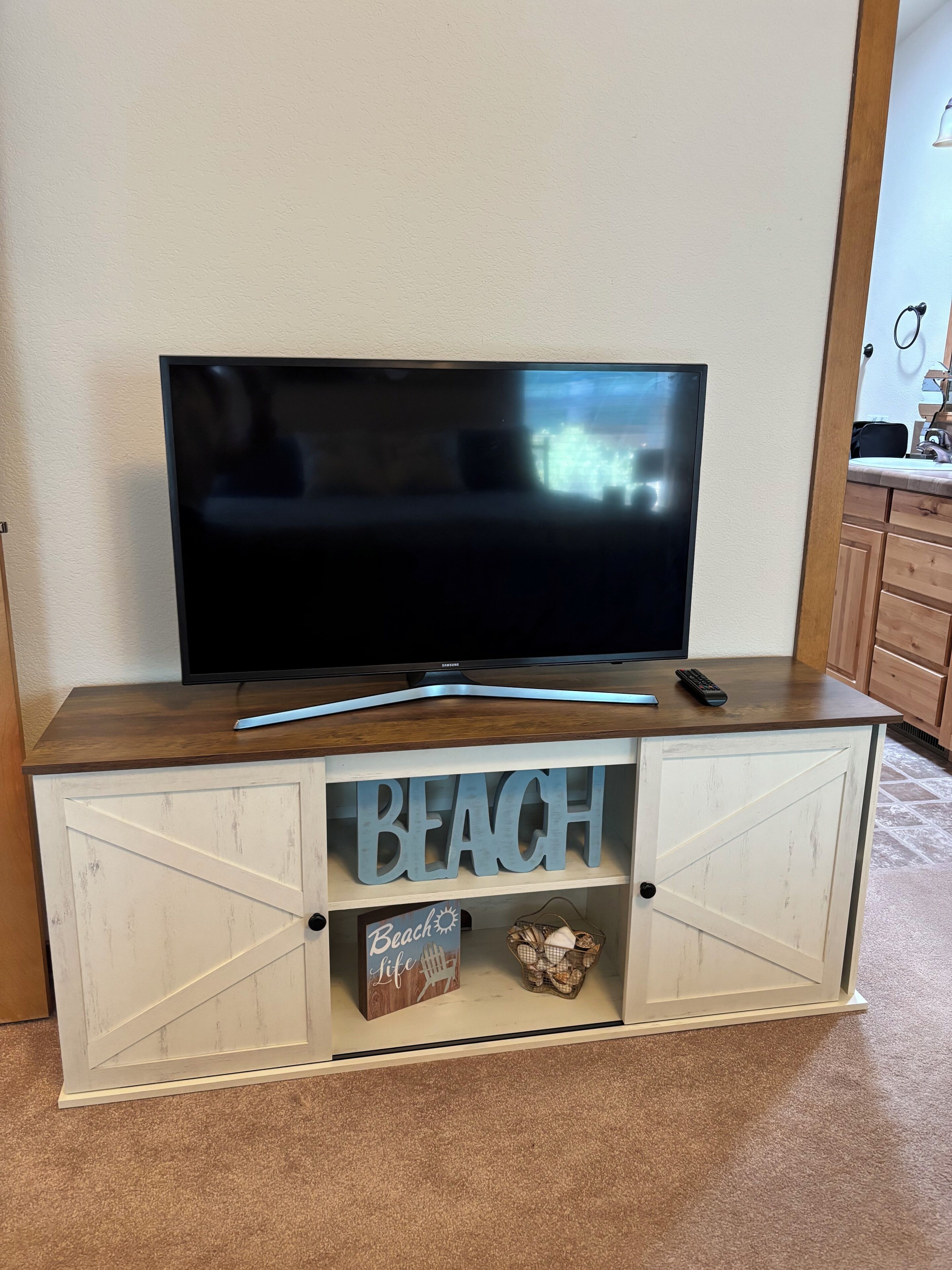 A flat-screen TV on a wooden cabinet with a 'BEACH' sign and a 'Beach Life' sign below.