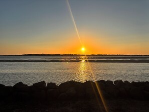 Un atardecer sobre una masa de agua con una costa rocosa al frente.