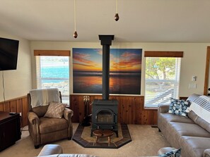 Una sala de estar con chimenea, dos sofás, un televisor y un cuadro grande de un atardecer.