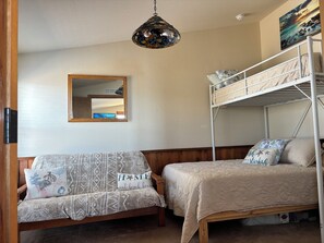 Un dormitorio con una cama litera, un sofá cama, un espejo y una lámpara colgante.
