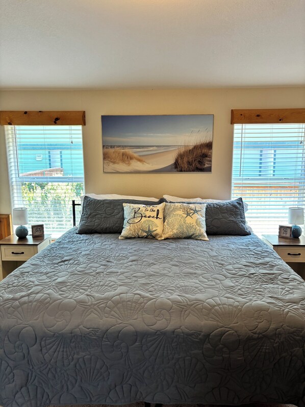 Un dormitorio con una cama grande, un cuadro de una playa y vistas al exterior por la ventana.