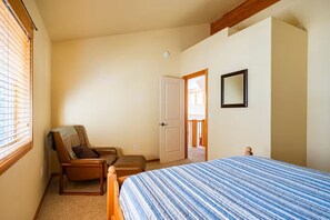 Ein Schlafzimmer mit einem Bett, einem Sessel, einer Tür und einem Fenster mit Jalousien.