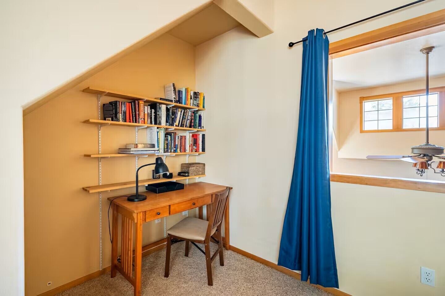 A study room with a desk, chair, bookshelves, and a window with curtains.