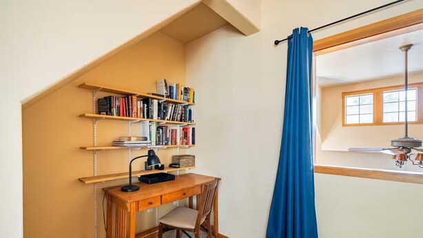 Una sala de estudio con escritorio, silla, estanterías y un ventanal con cortinas.